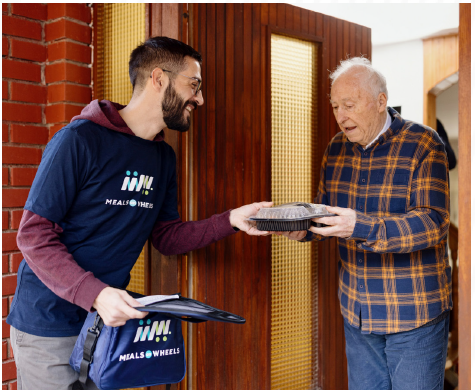 Meals on Wheels Volunteer handing a meal to a senior at their front door.